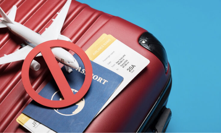 Luggage with a passport, toy airplane and a prohibition sign on top of it.