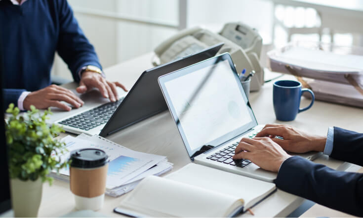 Two employees working with their laptops facing each other