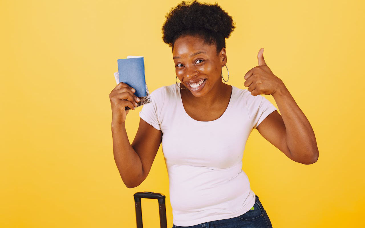 A woman showing thumbs up while holding passport and smiling at the camera.