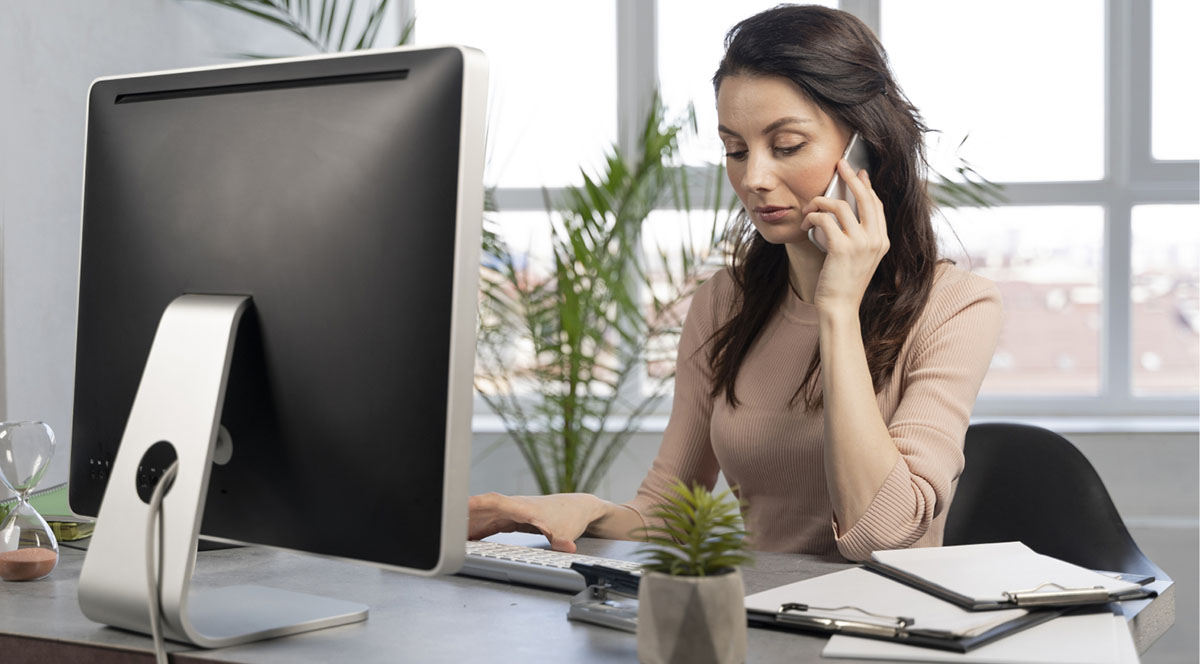 A woman with a serious face talking over phone in front of her computer table.