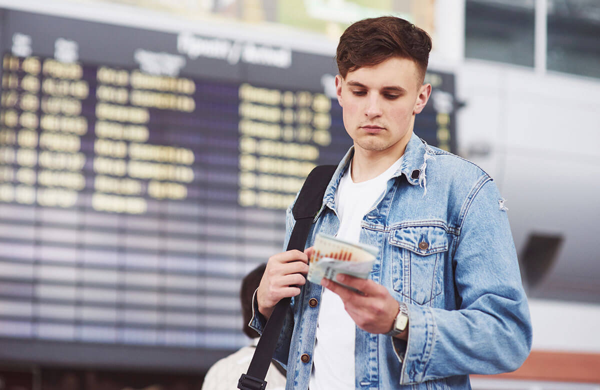 A male tourist at the airport looking at thing he is holding.