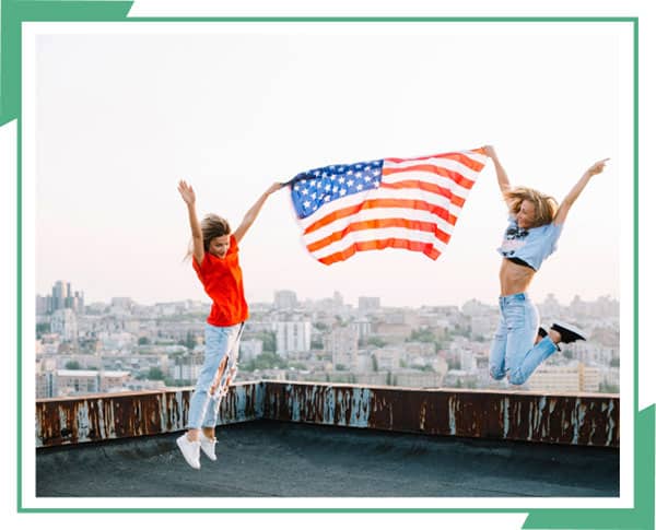 Two girls captured in jump shot while holding the American Flag.
