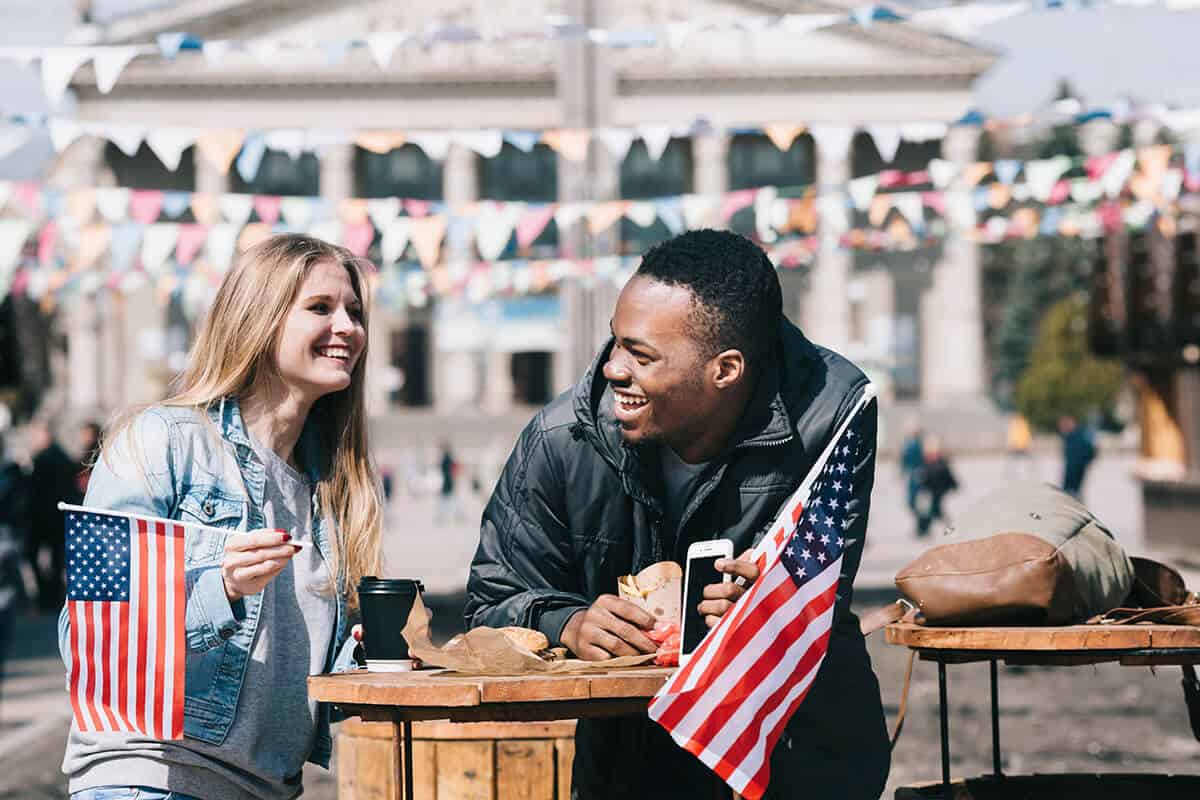 A man and woman outside talking while holding an American Flaglet