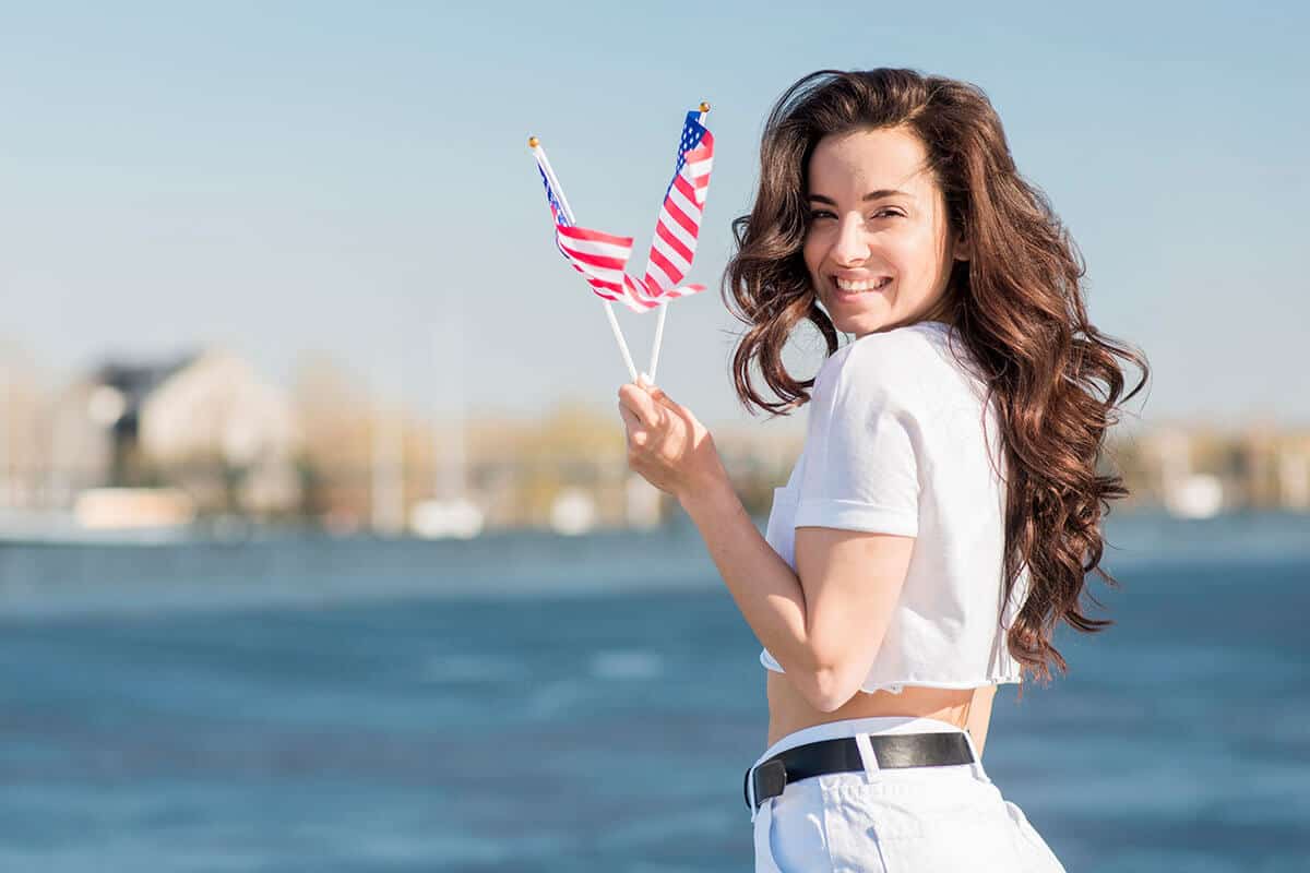 A woman in white top holding two American flaglets.