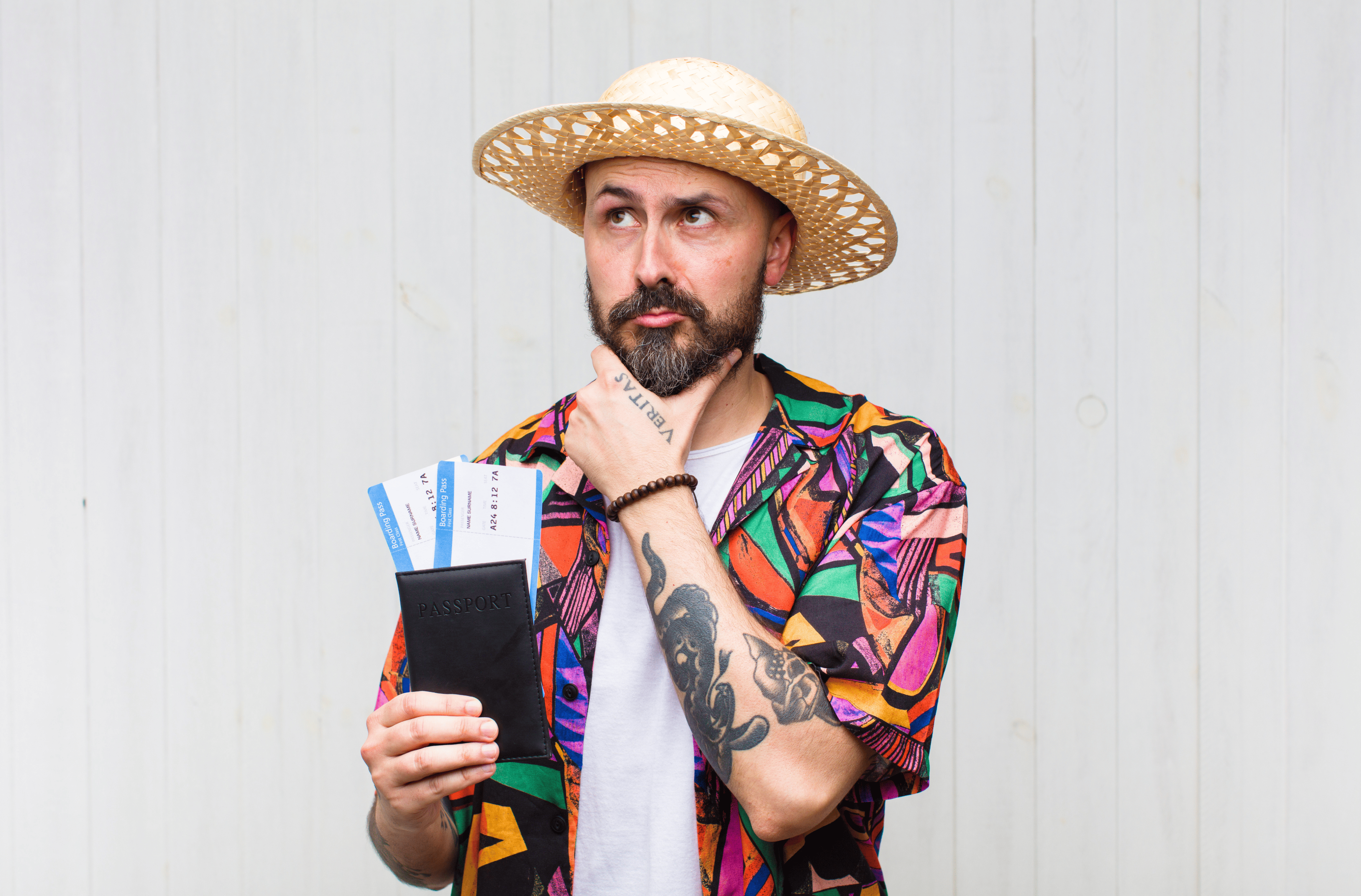 A man wearing a colorful polo, holding a passport and two plane tickets.